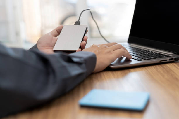 person using laptop and holding external drive