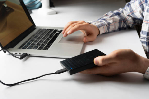 Person using a laptop holding an external drive